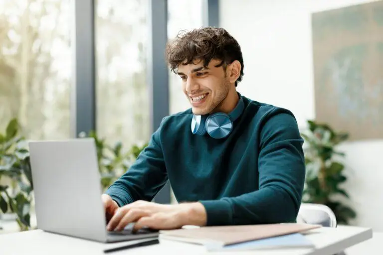 Vrolijke Europese kerel die laptop met behulp van, kijkend naar online les of webinar, zittend in moderne universiteit
